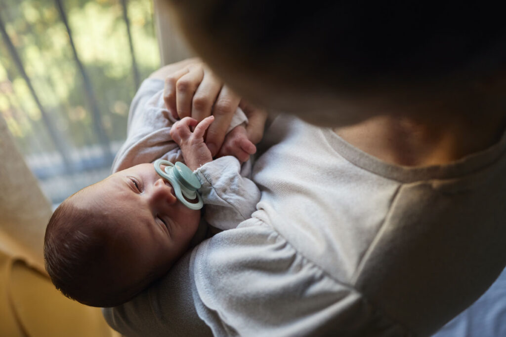 Baby with pacifier being held by parent near window