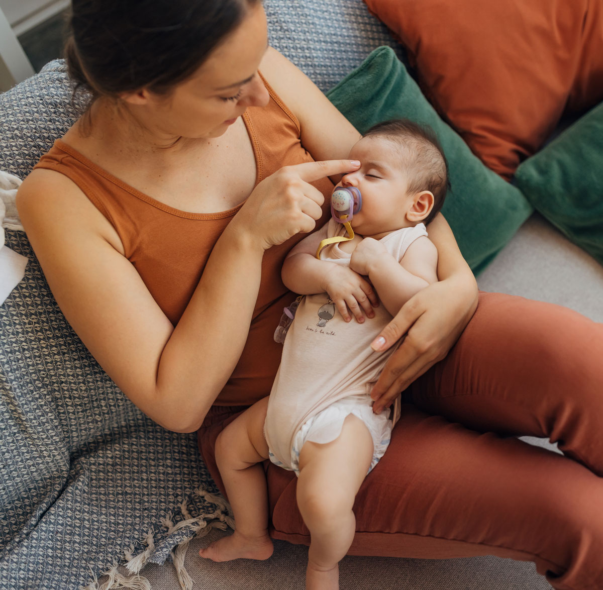 Mother holding a sleeping baby with a pacifier while sitting on a couch