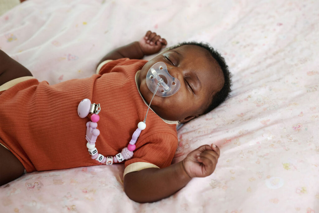 Sleeping baby with pacifier clip lying on pink blanket