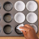 Hand greasing a muffin tray with cupcake liners
