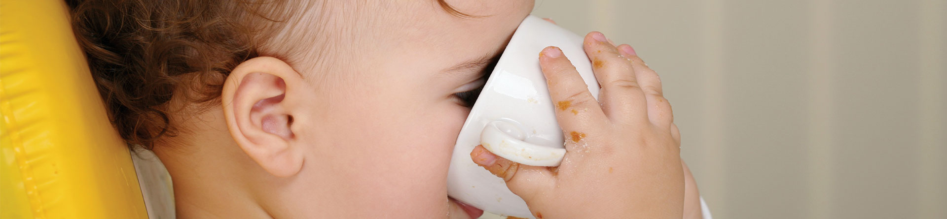 Toddler drinking from white cup, face partially visible.