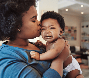 Parent comforting crying baby with gentle kiss