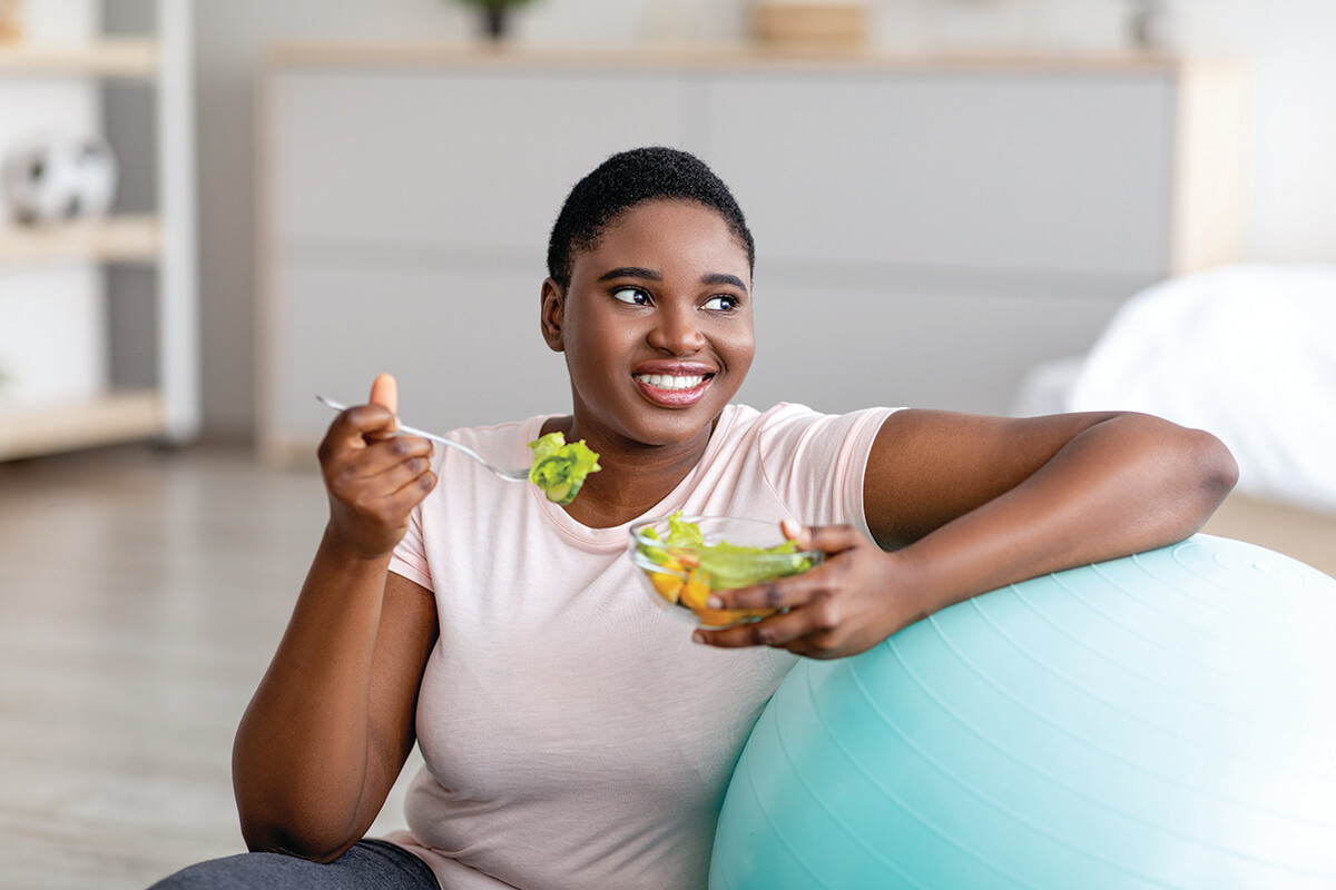 Woman smiling, eating salad beside exercise ball