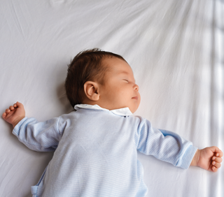 Sleeping baby in blue pajamas on white sheet