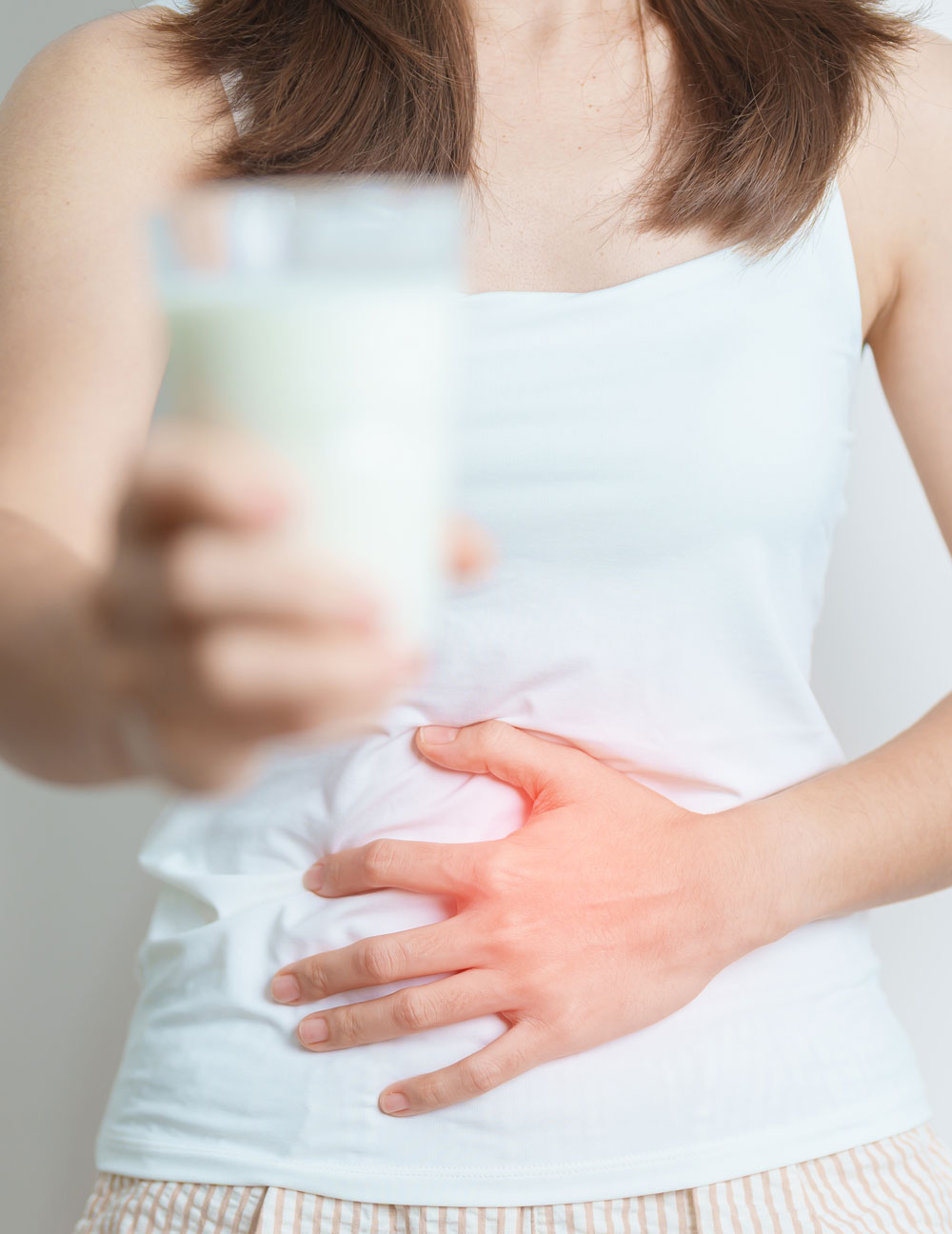 Person holding stomach in pain, holding glass of milk