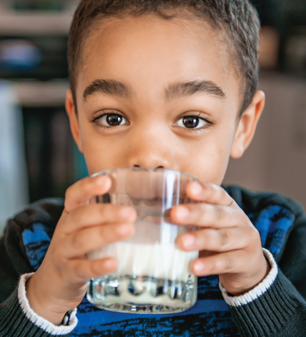 Child drinking milk from clear glass, looking forward