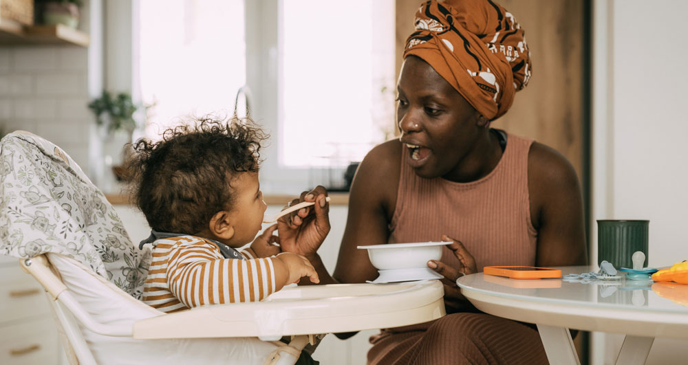 Mother feeding toddler in high chair, both smiling