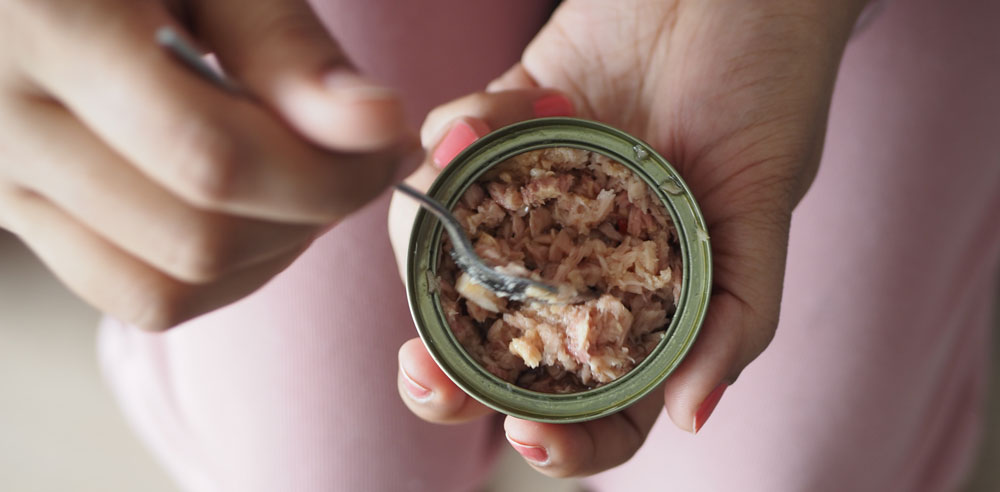 Hand holding canned tuna, stirring with a fork