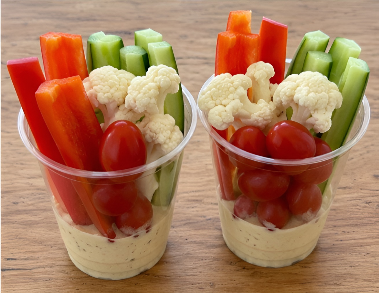 Two cups filled with fresh vegetables and hummus
