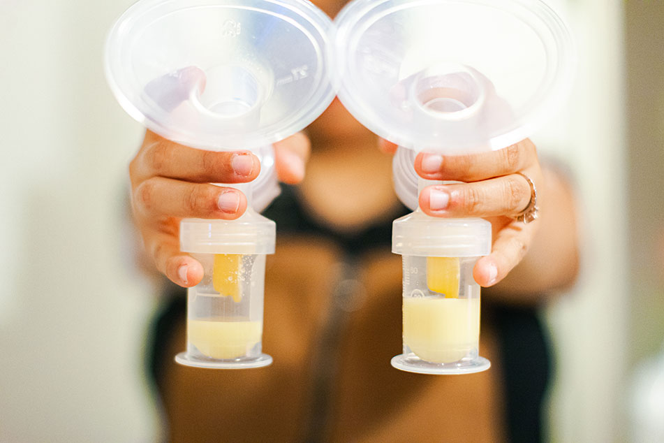 Hands holding breast pump bottles with milk.