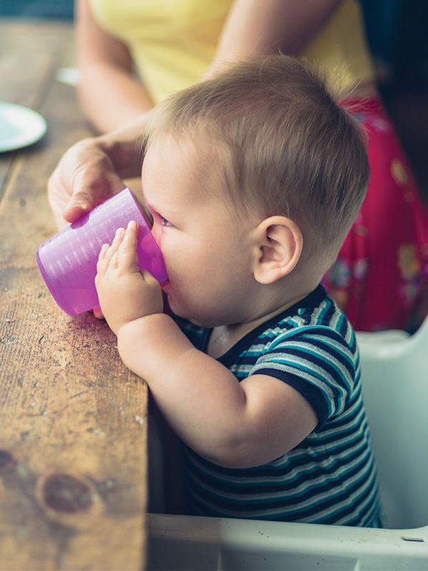 Baby drinking from purple cup at table.