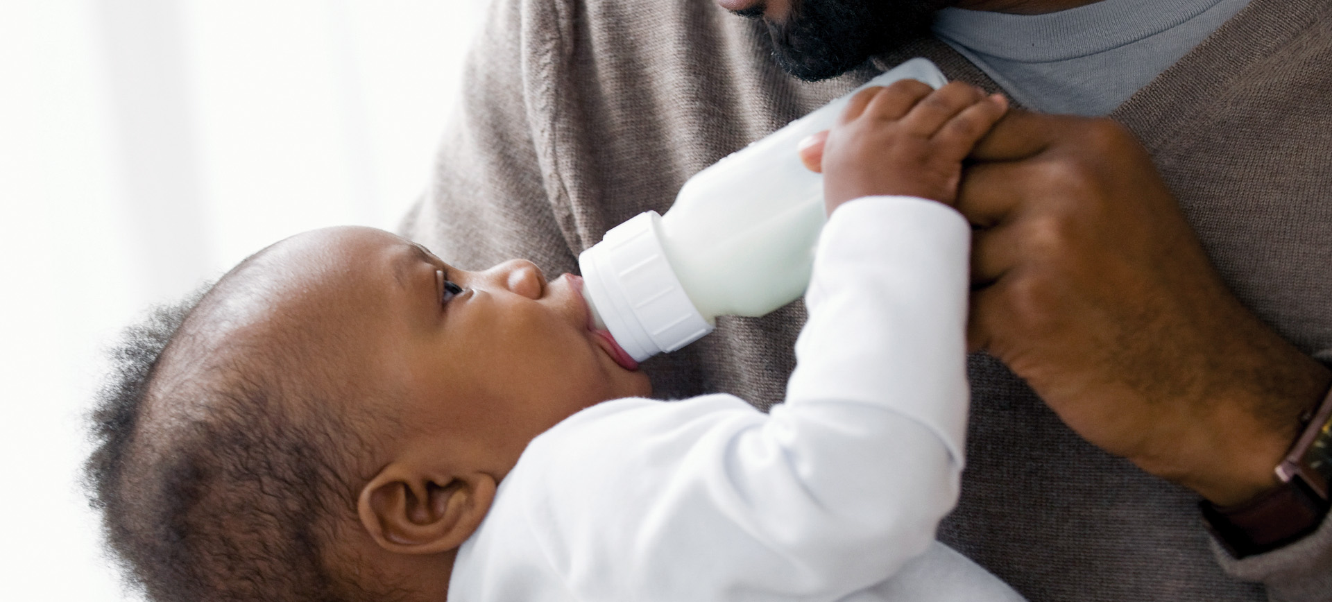 Baby drinking from bottle, held by adult.