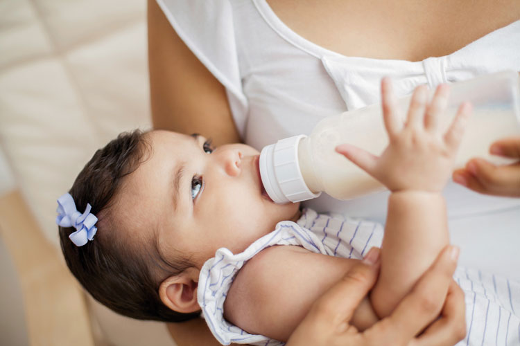 Baby drinking from bottle, held in caregivers arms