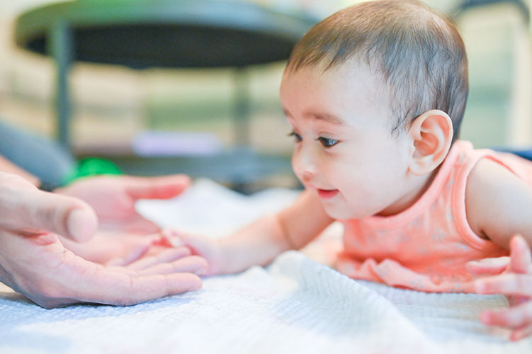 Baby reaching towards outstretched hand on blanket