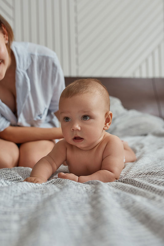 Baby lying on bed with parent nearby, observing