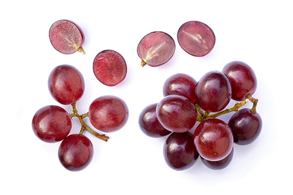 Red grapes and sliced halves arranged on white background