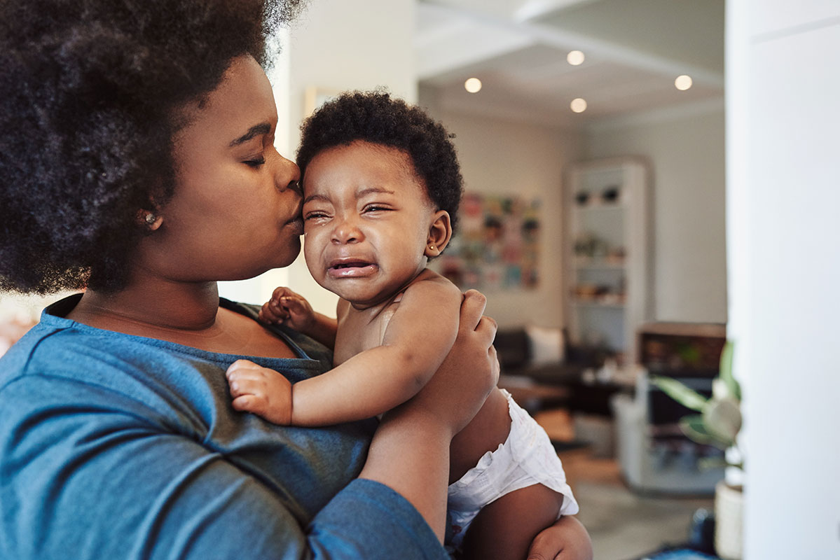 Mother kisses and comforts crying baby.