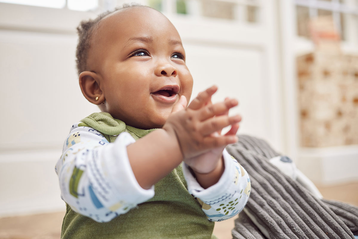 Smiling baby clapping hands joyfully indoors.