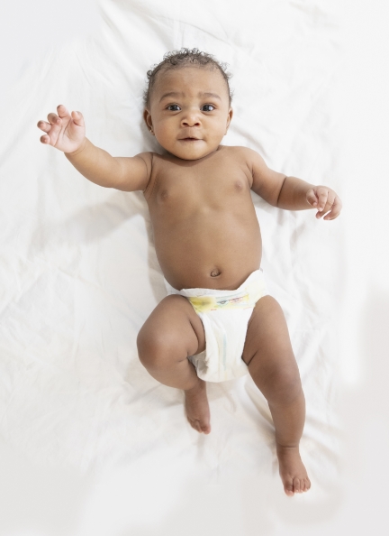 Baby lying on white sheet, reaching upward.