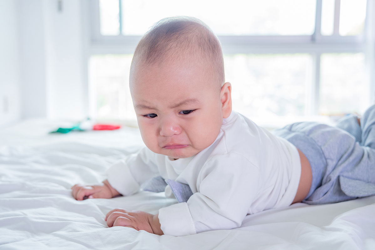 Baby lying on bed, looking upset.