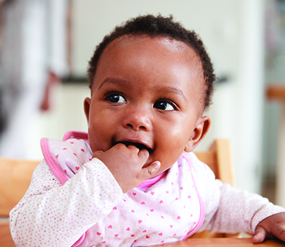 Baby chewing fingers while seated in high chair